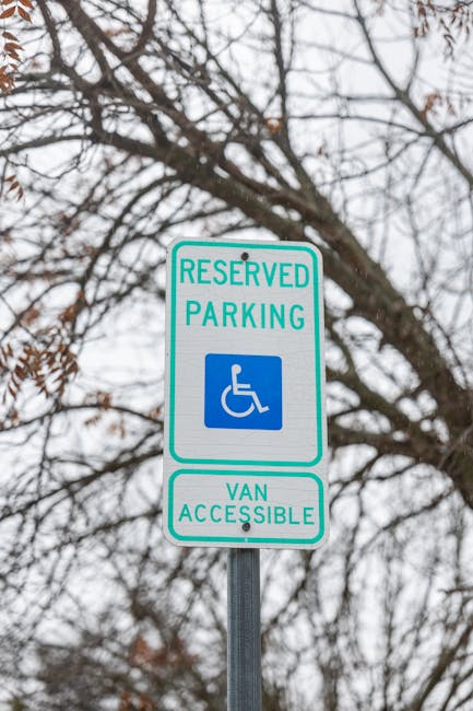 A green and white reserved parking sign designated for disabled individuals and vans, mounted on a metal pole outdoors. The sign features the wheelchair symbol and the texts 'RESERVED PARKING' and 'VAN ACCESSIBLE,' positioned against a backdrop of leafless tree branches and an overcast sky. This sign indicates parking restrictions applicable to nearby areas used for home relocation and furniture transport during moving and removal services. Such signage is relevant to the logistics of house removals, ensuring accessible parking for vans involved in packing and loading processes, as handled by Man and Van Lambeth, a professional removals company specializing in local and long-distance moves.